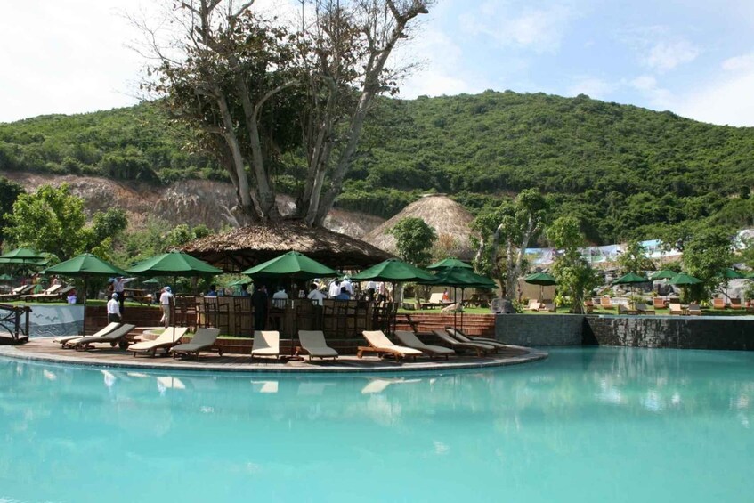 A pool with lounge chairs and umbrellas, surrounded by lush greenery and a hill in the background. 2