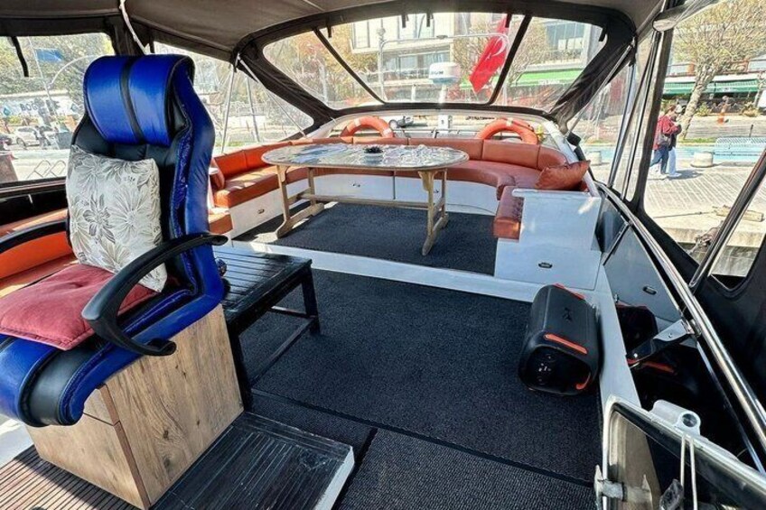 A boat interior with a blue and red cushioned seating area, a small table, and a steering wheel. 4