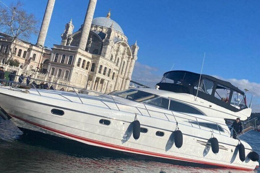 A white yacht with a red stripe, docked near a historic building with columns and a dome. 1