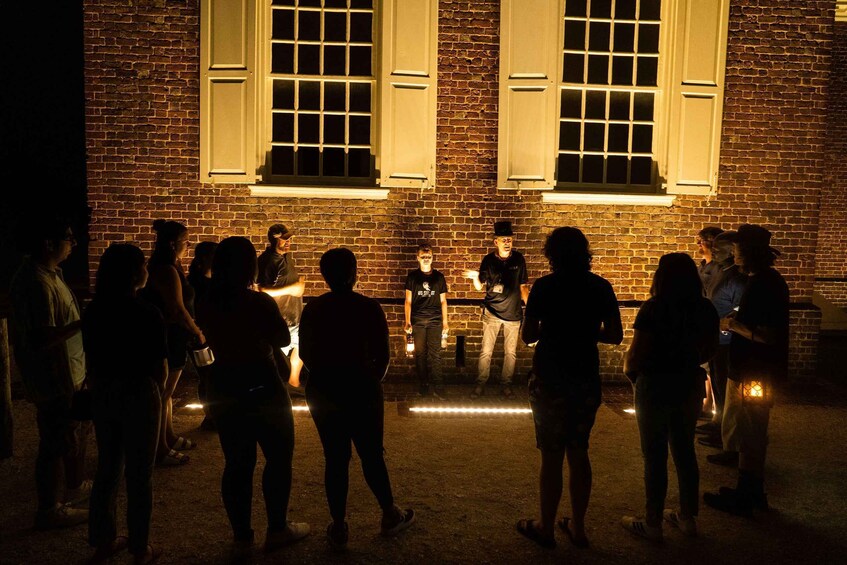 A group of people standing in front of a brick building with large windows and a brick wall. 4