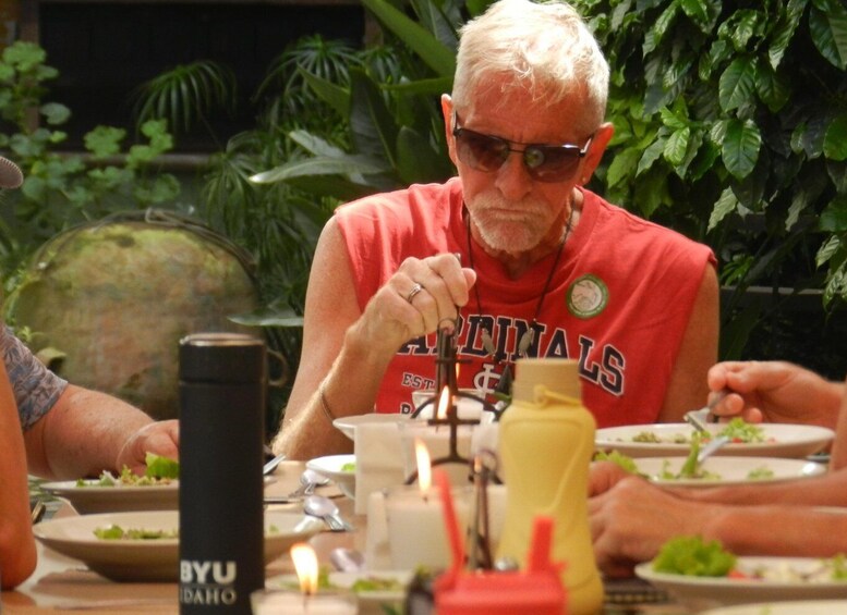 A person wearing a red Cardinals t-shirt sitting at a table with food, a black BYU Idaho water bottle, and a yellow condiment bottle. 2