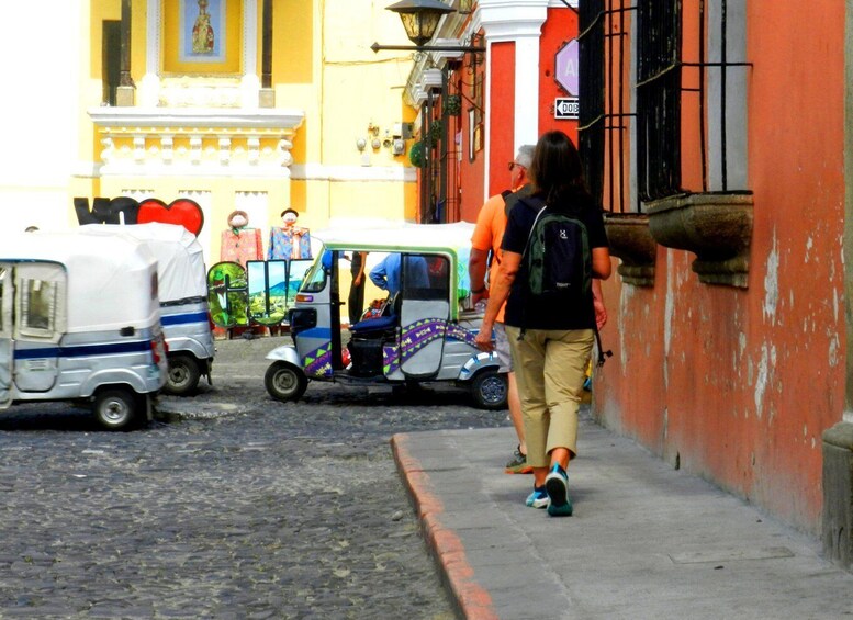 A narrow street with tuk-tuks and a pedestrian walking by a building with a red wall and a sign that reads 'A'. 4