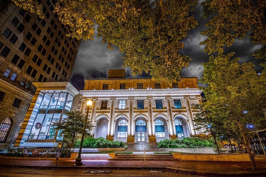 A historic building with large windows and a central entrance, surrounded by trees and a wet street. 4