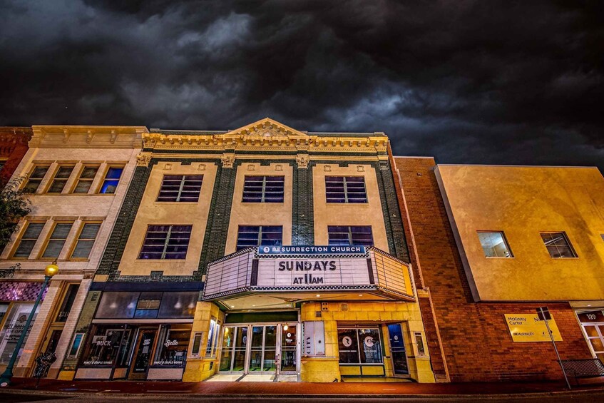 A theater with 'Sundays at 11am' sign, adjacent to a McKinley Carter store, under a dark sky. 1