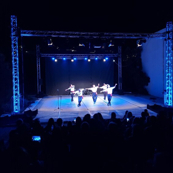 A stage with performers in white shirts and black pants, illuminated by blue stage lights. 2
