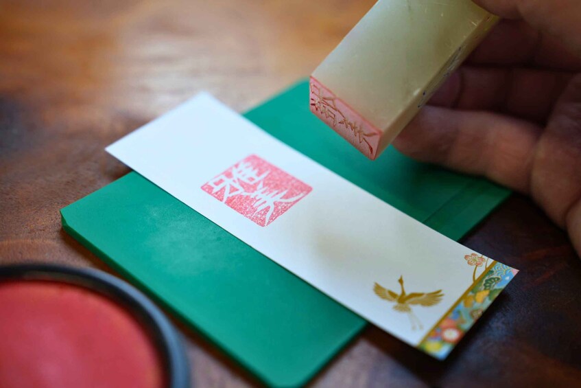 A hand stamping a red seal onto a white envelope with a green background. 1