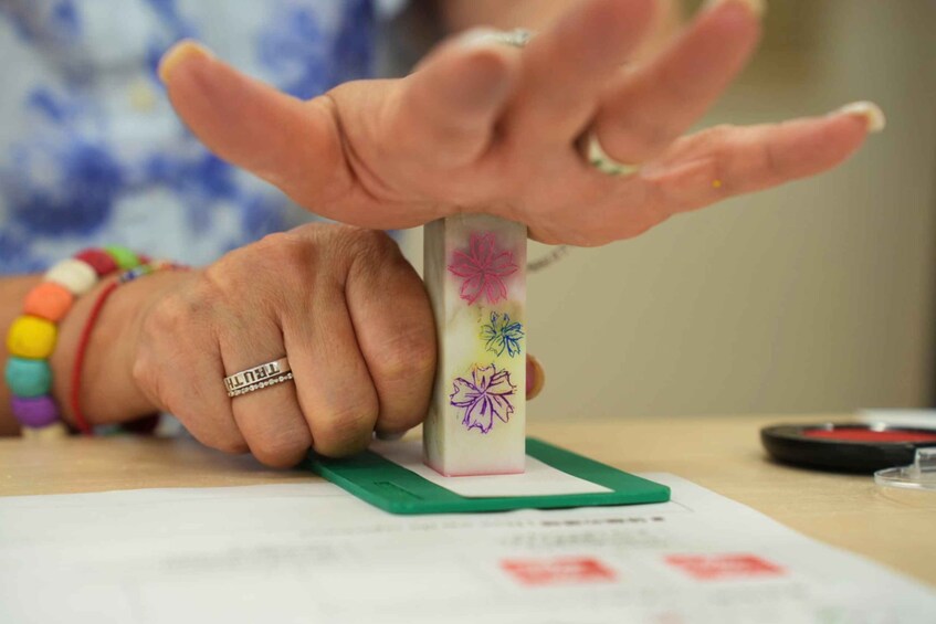 A hand holding a rectangular object with floral designs, placed on a green base. 2