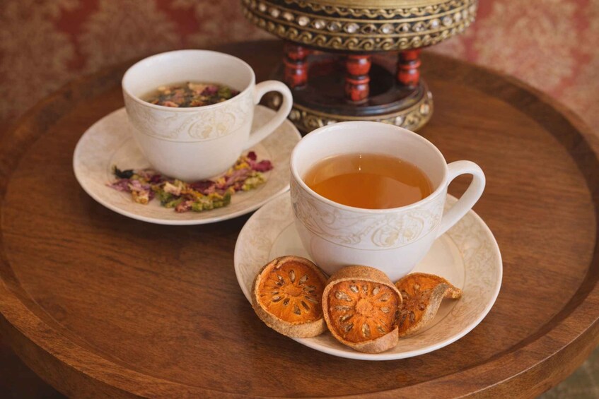 Two white cups of tea with floral patterns on saucers, a wooden tray, and dried fruit slices. 4