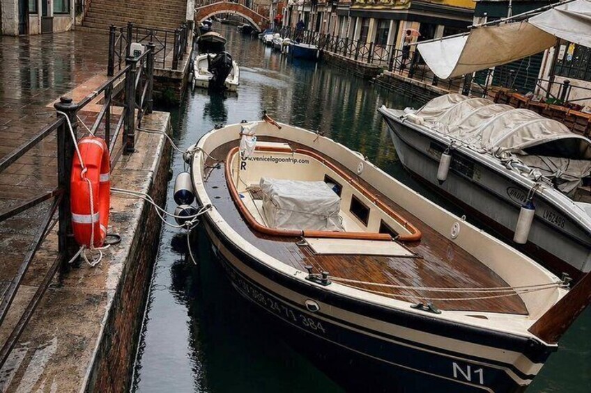 A narrow canal with boats docked, a lifebuoy, and a bridge in the background. 5