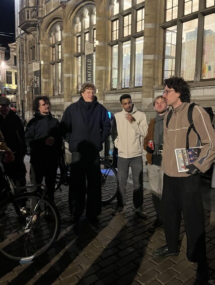 A group of people standing on a cobblestone street at night, with a historic building in the background. 4