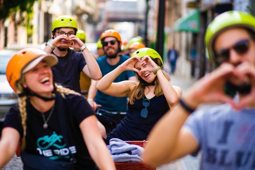 A group of people on a tandem bike, wearing helmets and casual clothing, on a city street. 3