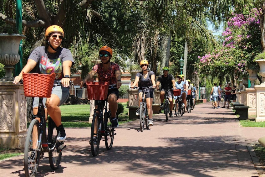 People riding bicycles on a paved path surrounded by palm trees and flowers. 1