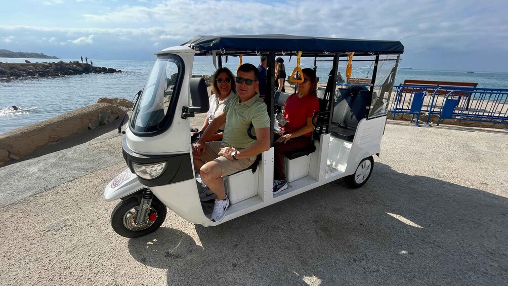 A three-seater vehicle parked by a waterfront with a rocky breakwater and the sea in the background. 4