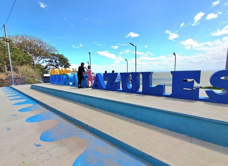 Large blue letters spelling 'VENEZUELA' on a seaside promenade with a clear sky and ocean in the background. 3