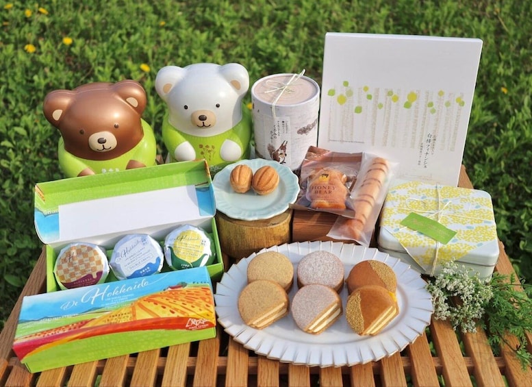A picnic setup with a teddy bear, candles, a card, and various food items on a wooden table. 1