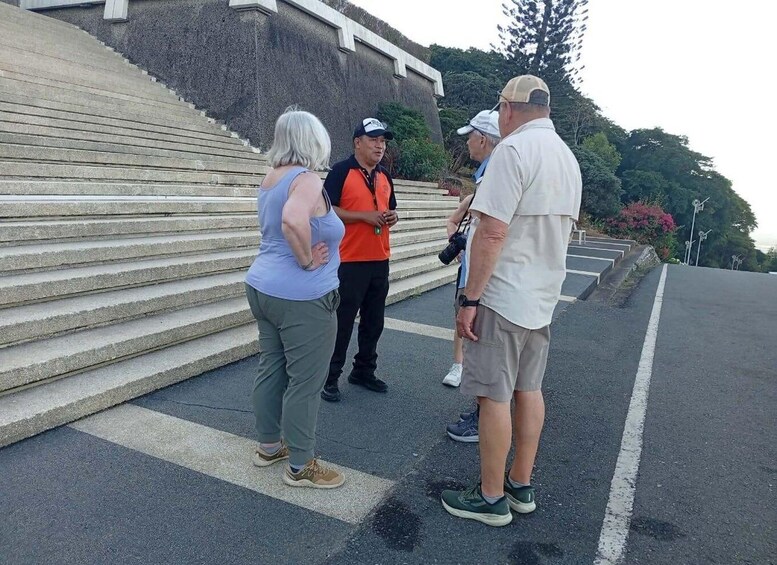 A group of people standing on a set of concrete steps with a road and greenery in the background. 1