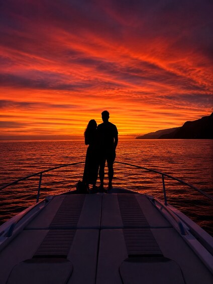 A couple silhouetted against a sunset on a boat. 1