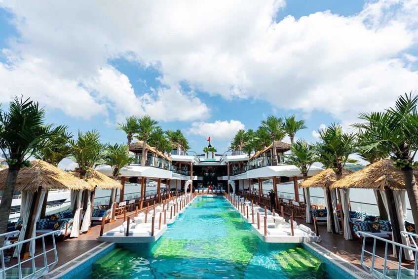 A cruise ship deck with a central pool, lounge chairs, palm trees, and a clear sky. 2