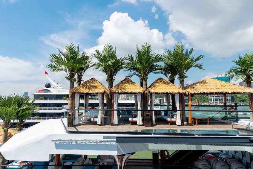 A cruise ship deck with thatched-roof cabanas, palm trees, and a swimming pool. 4