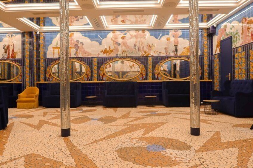 A luxurious restroom with ornate mirrors, a patterned floor, and a mural of dancers. 2