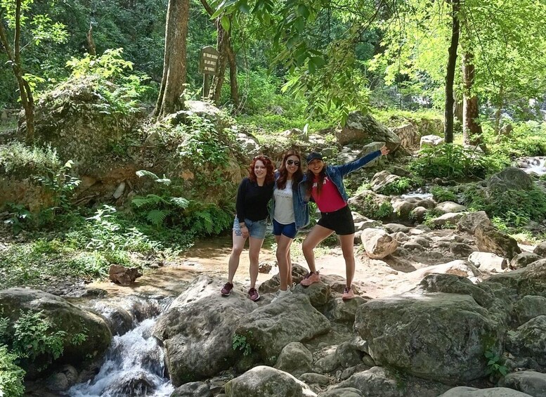 Three people standing on rocks by a waterfall in a forested area. 3