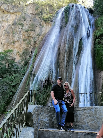 A couple sitting on a stone ledge with a waterfall in the background. 1