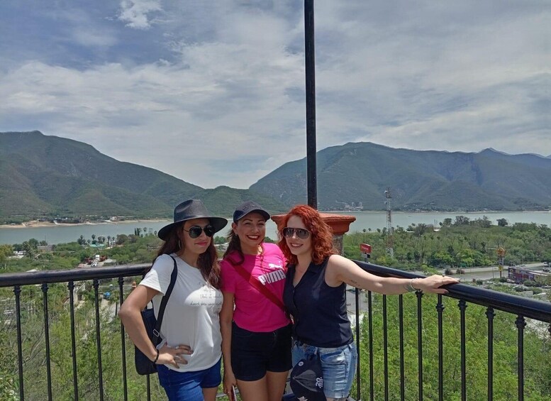 Three people standing on a balcony with a scenic view of mountains and a body of water. 4