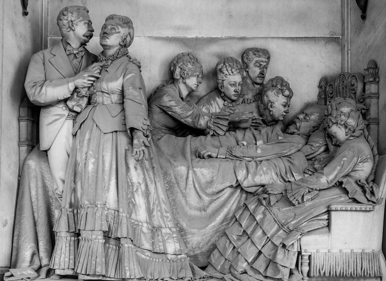 A detailed stone sculpture of a historical scene with figures in period attire, a central reclining figure, and a backdrop of architectural elements. 4