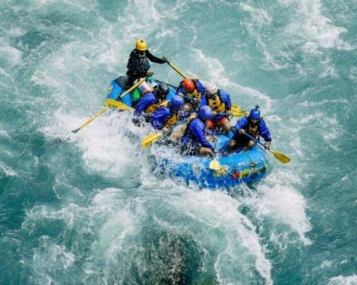 A group of people in a blue raft navigating through turbulent water. 1