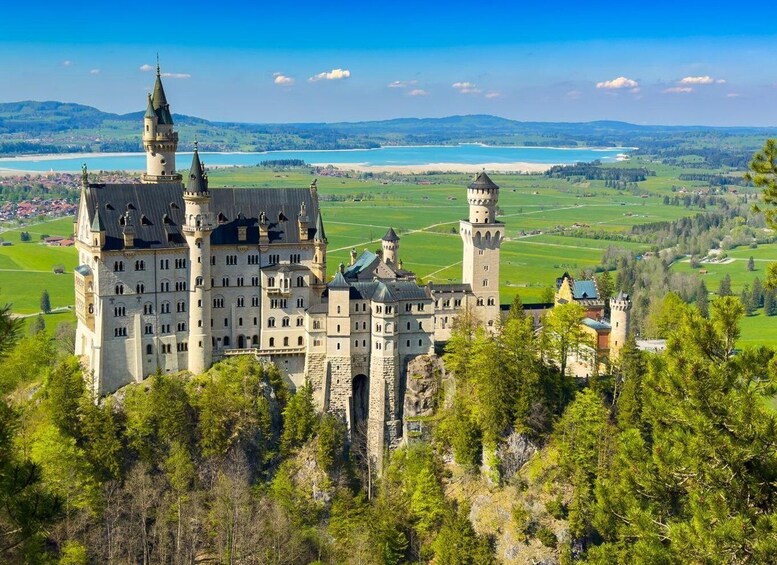 A historic castle with multiple towers, surrounded by lush greenery and a scenic landscape with a lake in the background. 4