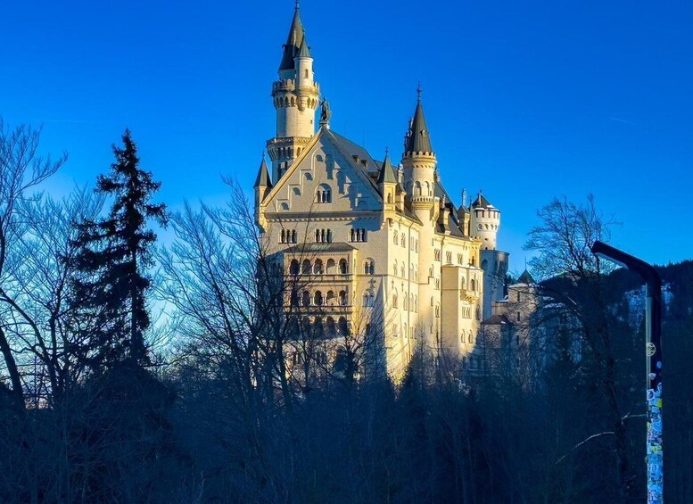 A large, historic castle with multiple towers and a prominent central tower, surrounded by trees and a clear sky. 2
