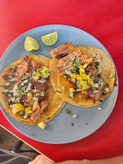 Two tacos with meat and diced onions on a blue plate, accompanied by lime wedges. 3
