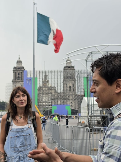 A person gesturing towards a historic building with a flag, a person in denim overalls, and a cityscape in the background. 4