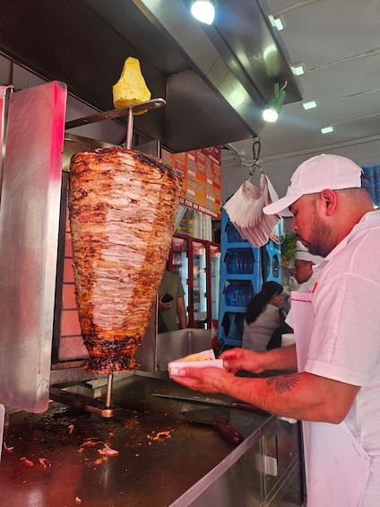 A man preparing food at a vertical rotisserie with a menu in the background. 2