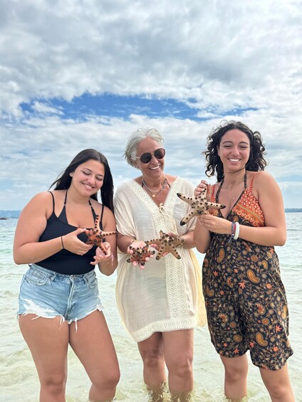 Three people holding starfish at a beach with clear skies. 5