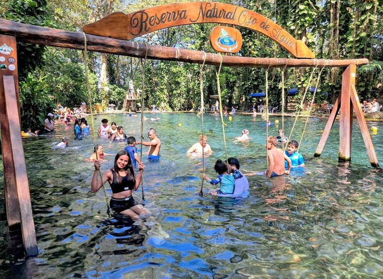 A natural pool with people swimming and playing, surrounded by lush greenery. 2