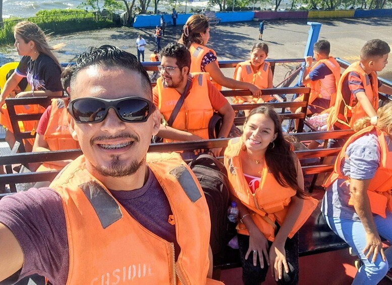 A group of people wearing orange vests, seated on a structure with metal railings. 5
