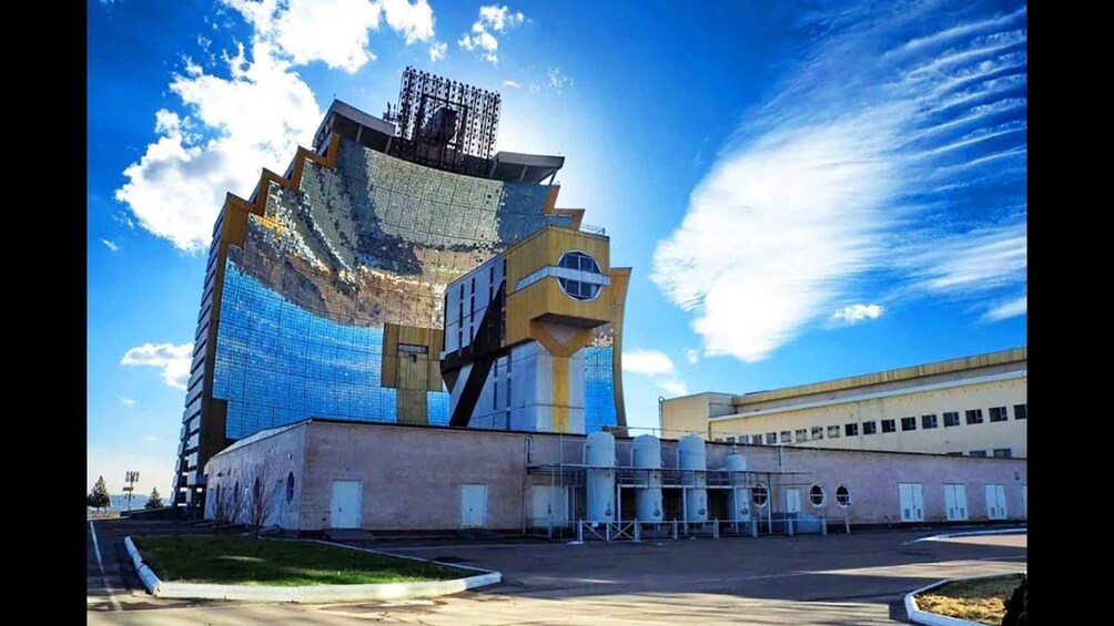 A large, uniquely designed building with a curved facade and a prominent yellow structure on the right. 1