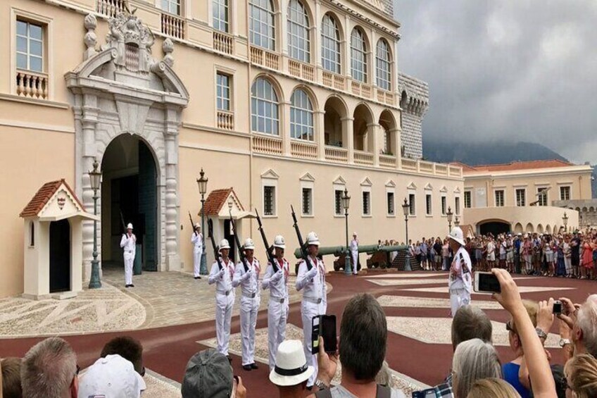 A military parade with soldiers in white uniforms and hats, standing in formation in front of a historic building with arches and columns. 2