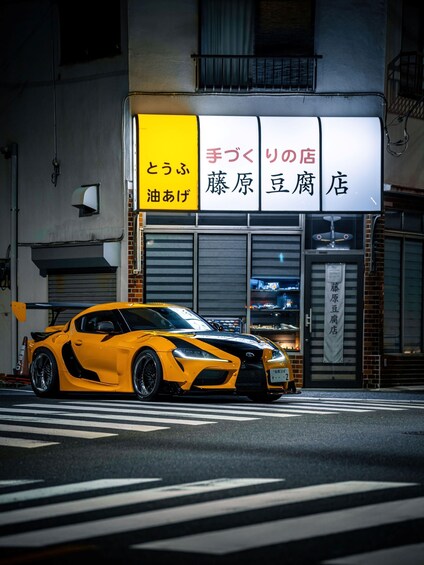 En gul sportsvogn parkeret foran en bygning med et skilt på japansk. 4