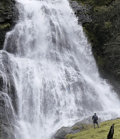 A waterfall with a person standing on a grassy hill. 2