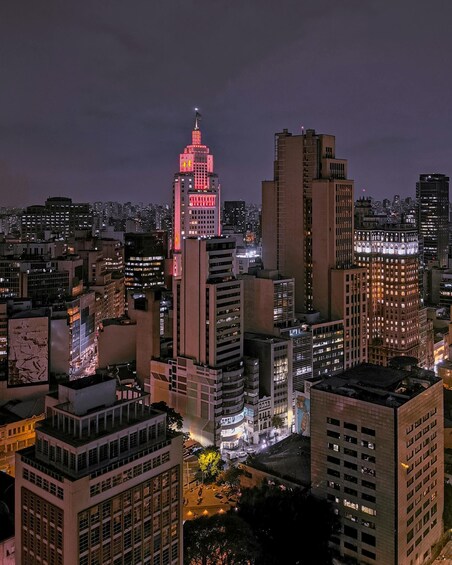 A cityscape at night with illuminated buildings and a prominent skyscraper with a flag on top. 2