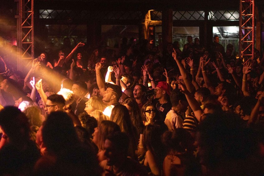 A crowd at an outdoor event with raised hands and stage lighting. 1