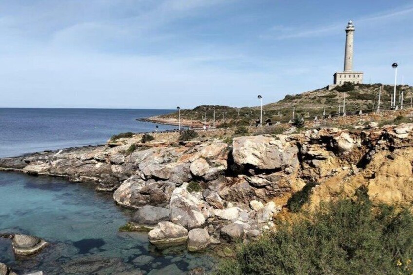 A rocky coastline with a lighthouse and clear blue sea. 4
