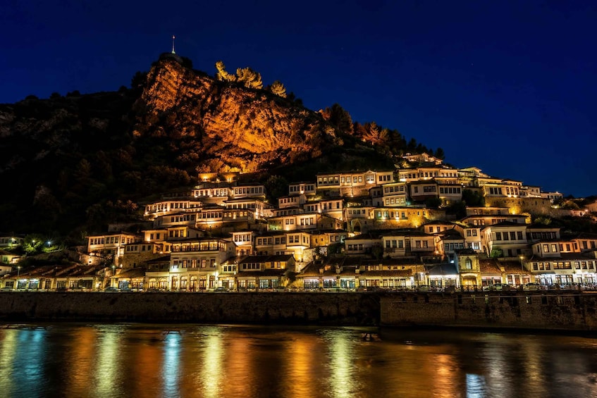 A night view of a coastal town with buildings illuminated against a mountain backdrop. 1