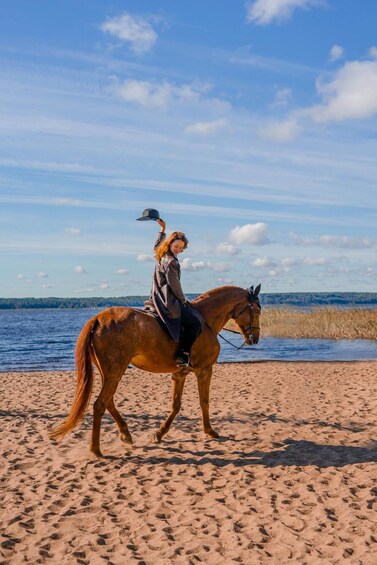 A person riding a horse on a sandy beach with water and trees in the background. 3
