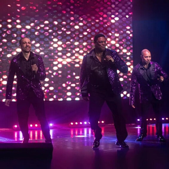 Three men performing on a stage with a backdrop of circular lights. 3
