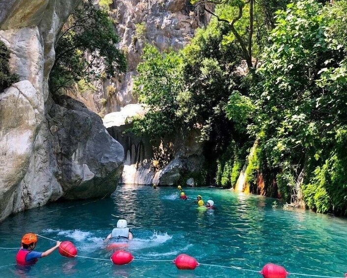 People water skiing in a river surrounded by cliffs and greenery. 4