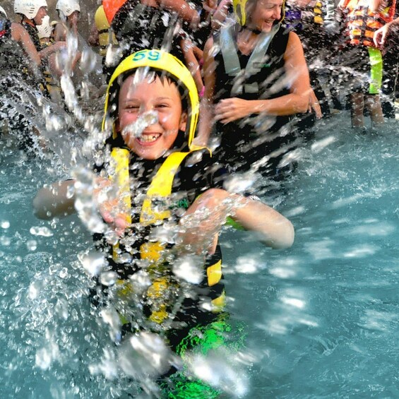 A child in a pool splashing water, wearing a yellow helmet and a life jacket. 2