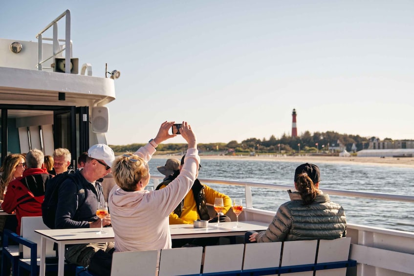 People on a boat, some taking photos, with a lighthouse in the background. 3